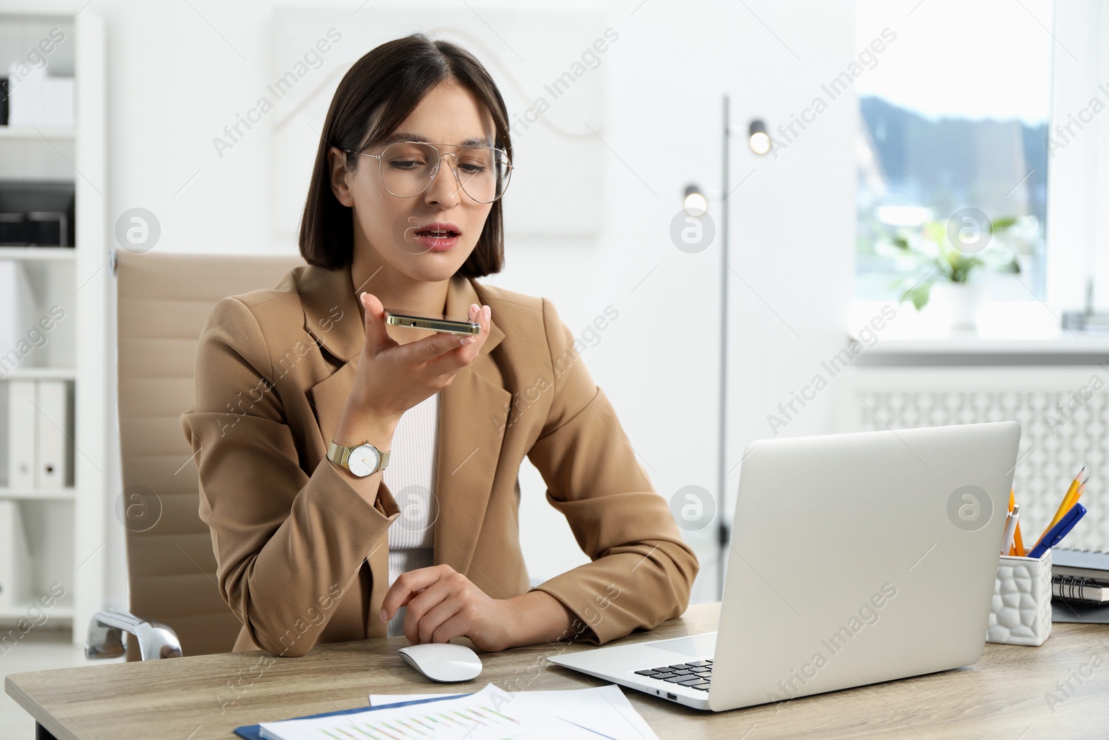 Photo of Beautiful woman recording voice message via smartphone in office