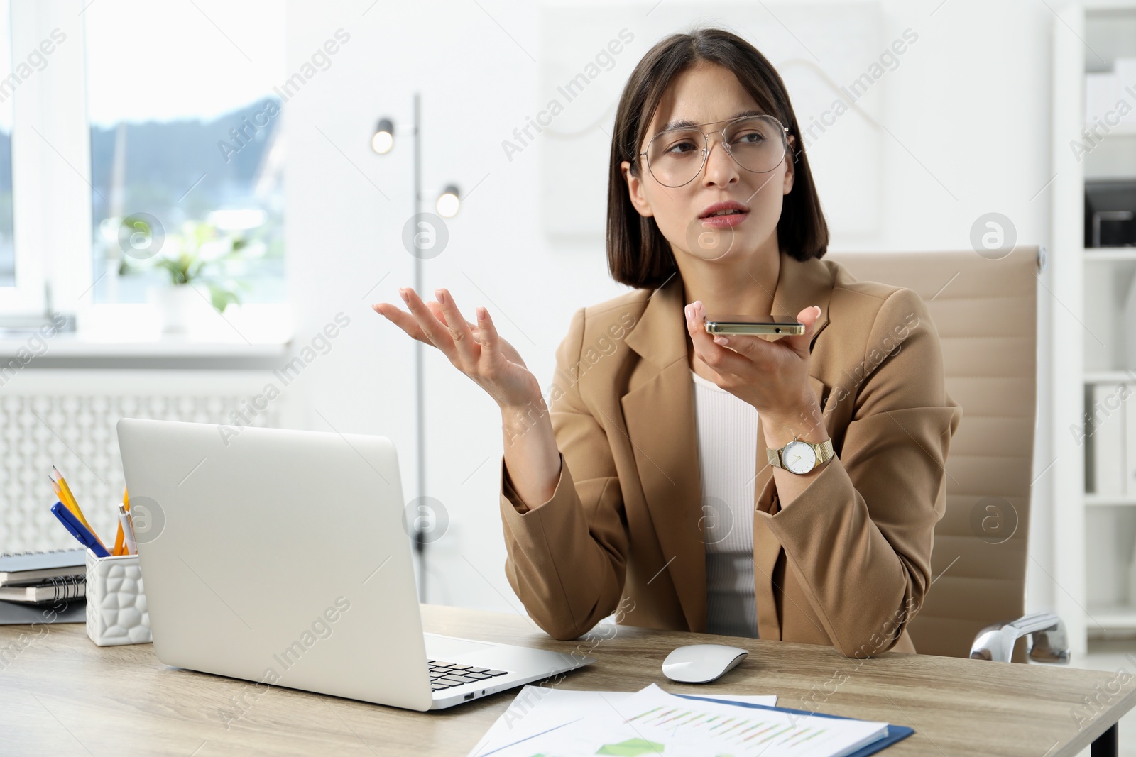 Photo of Beautiful woman recording voice message via smartphone in office