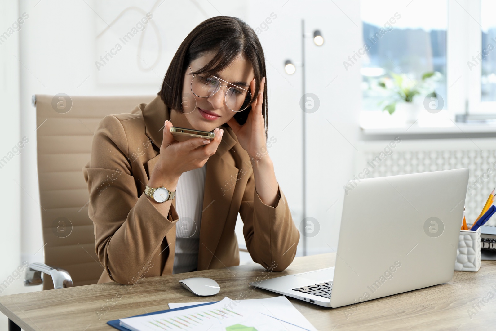 Photo of Beautiful woman recording voice message via smartphone in office