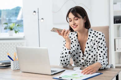 Photo of Beautiful woman recording voice message via smartphone in office