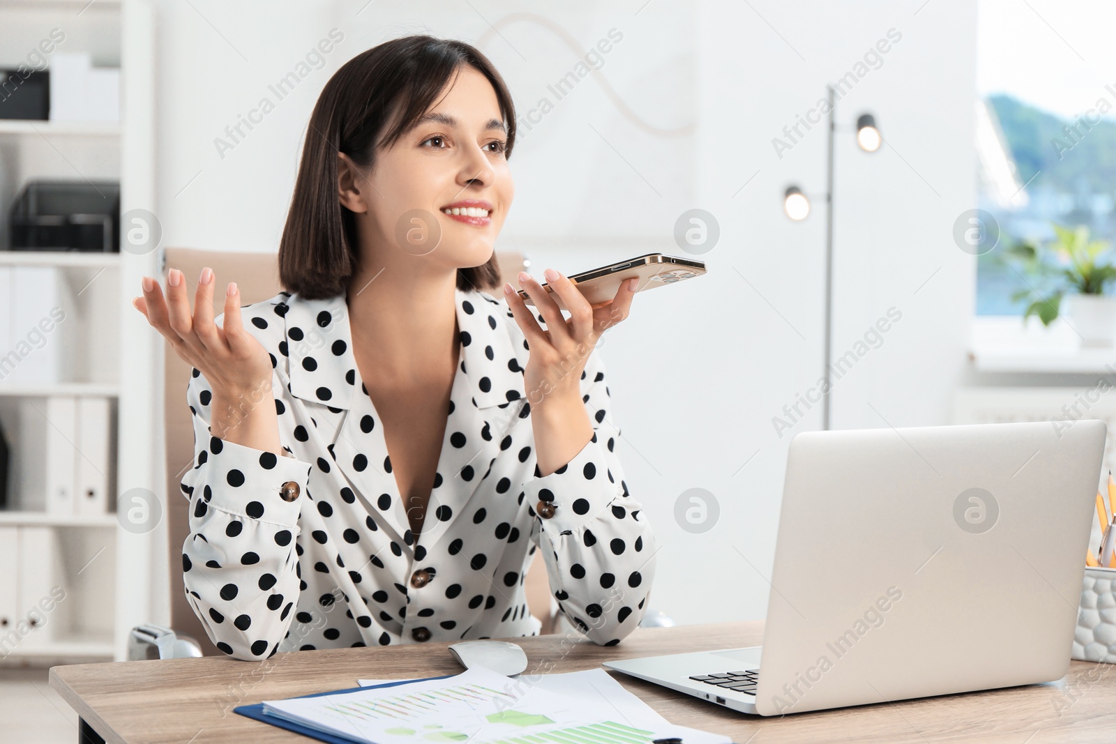 Photo of Beautiful woman recording voice message via smartphone in office