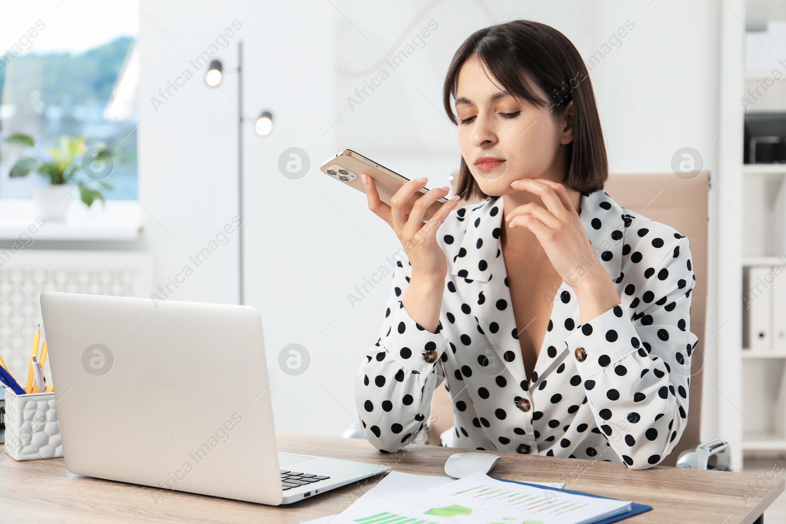 Photo of Beautiful woman recording voice message via smartphone in office