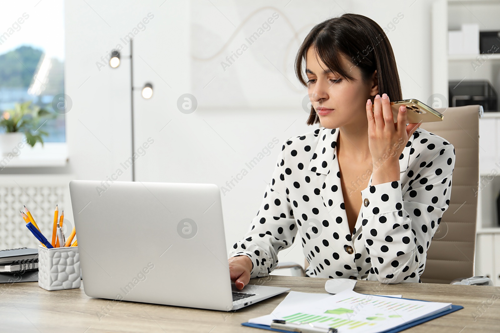 Photo of Beautiful woman with smartphone listening to voice message in office