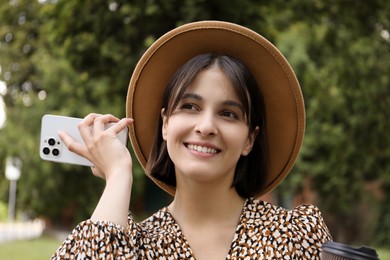 Photo of Beautiful woman with smartphone listening to voice message outdoors