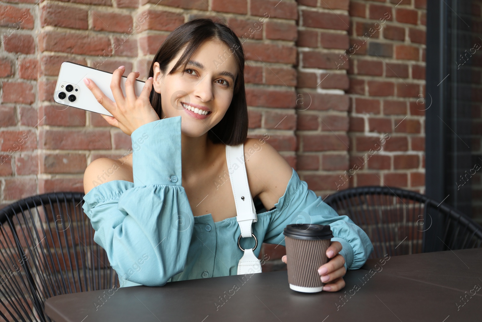 Photo of Beautiful woman with smartphone listening to voice message in outdoor cafe