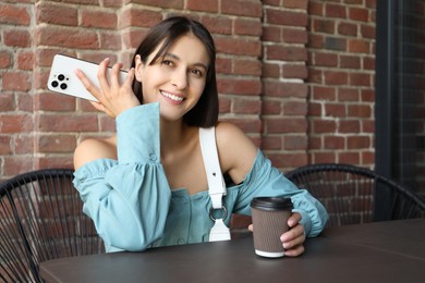 Photo of Beautiful woman with smartphone listening to voice message in outdoor cafe