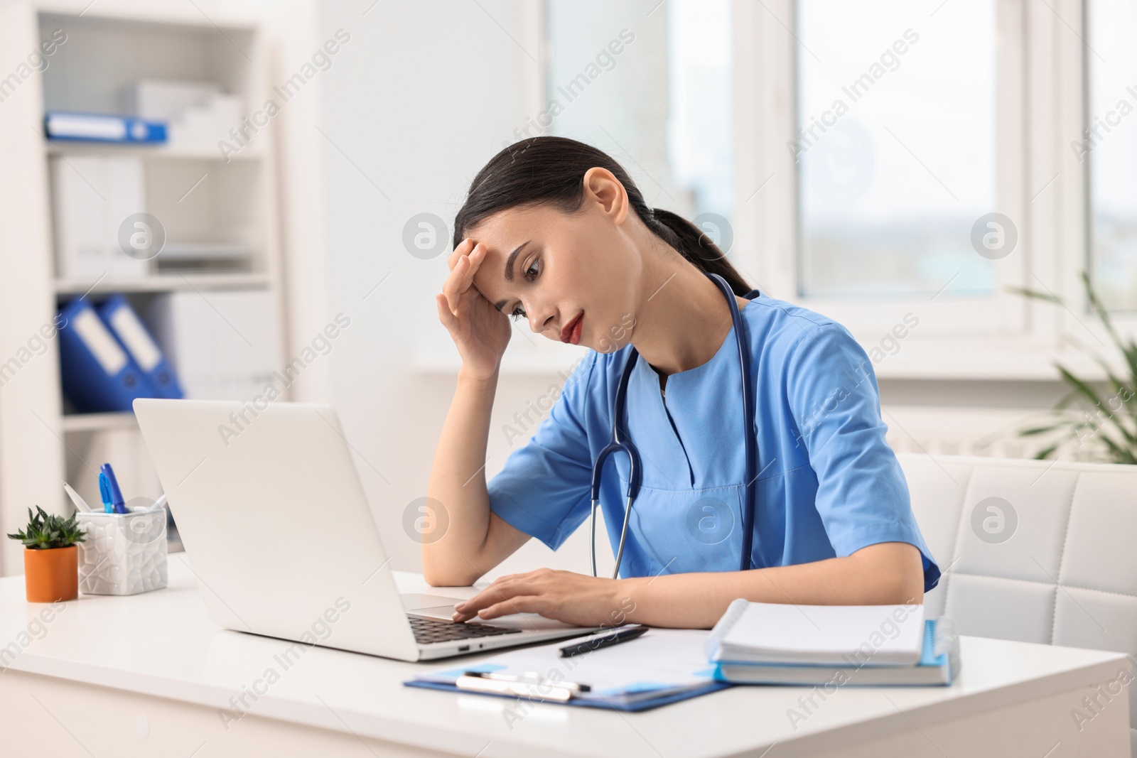 Photo of Tired nurse working with laptop at table in clinic