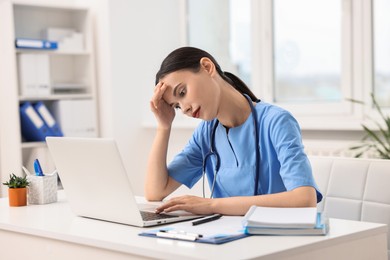 Tired nurse working with laptop at table in clinic