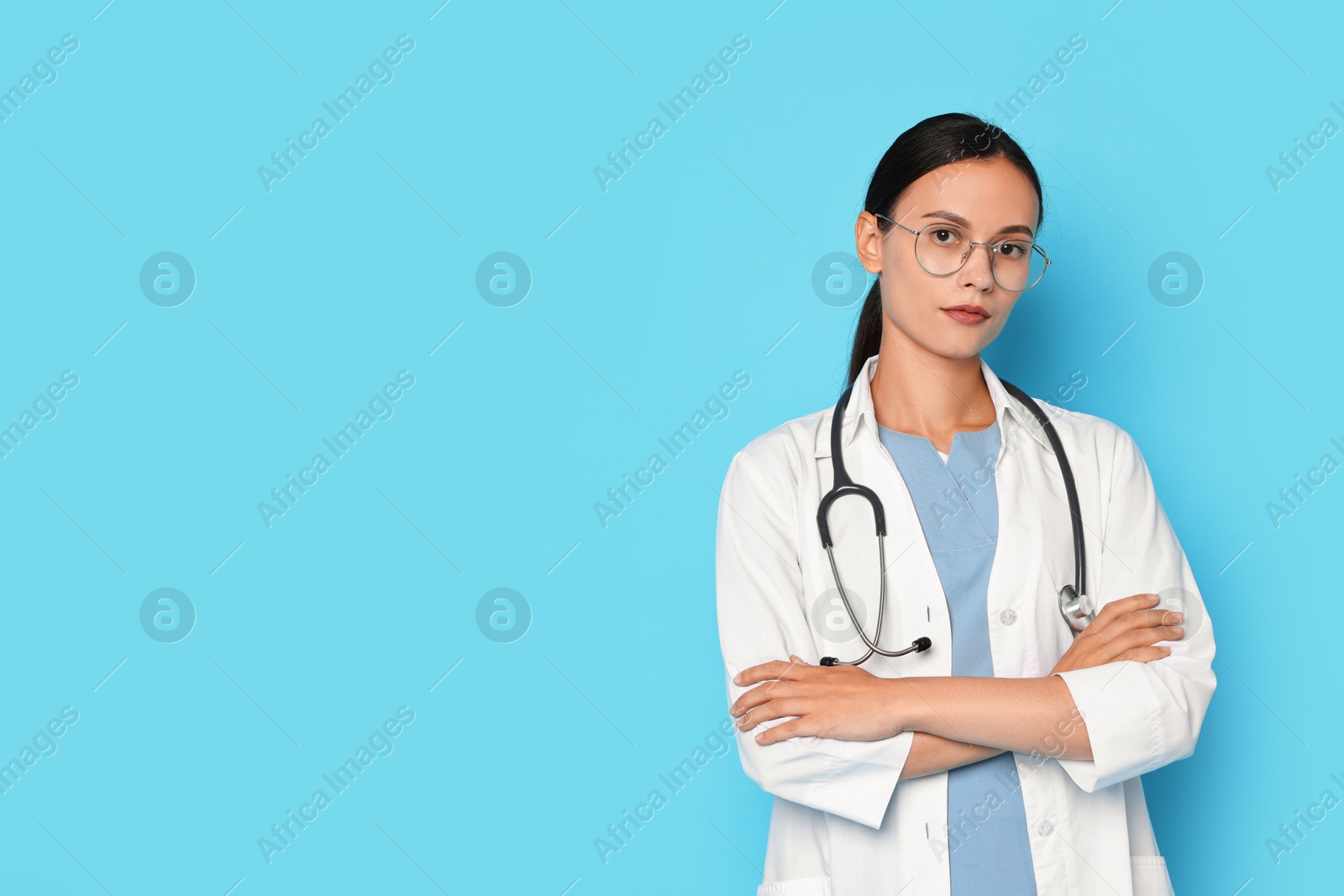 Photo of Beautiful nurse with crossed arms on light blue background. Space for text