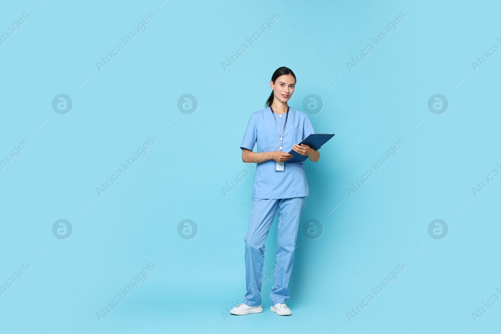 Photo of Beautiful nurse with clipboard on light blue background