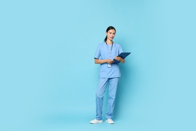 Beautiful nurse with clipboard on light blue background