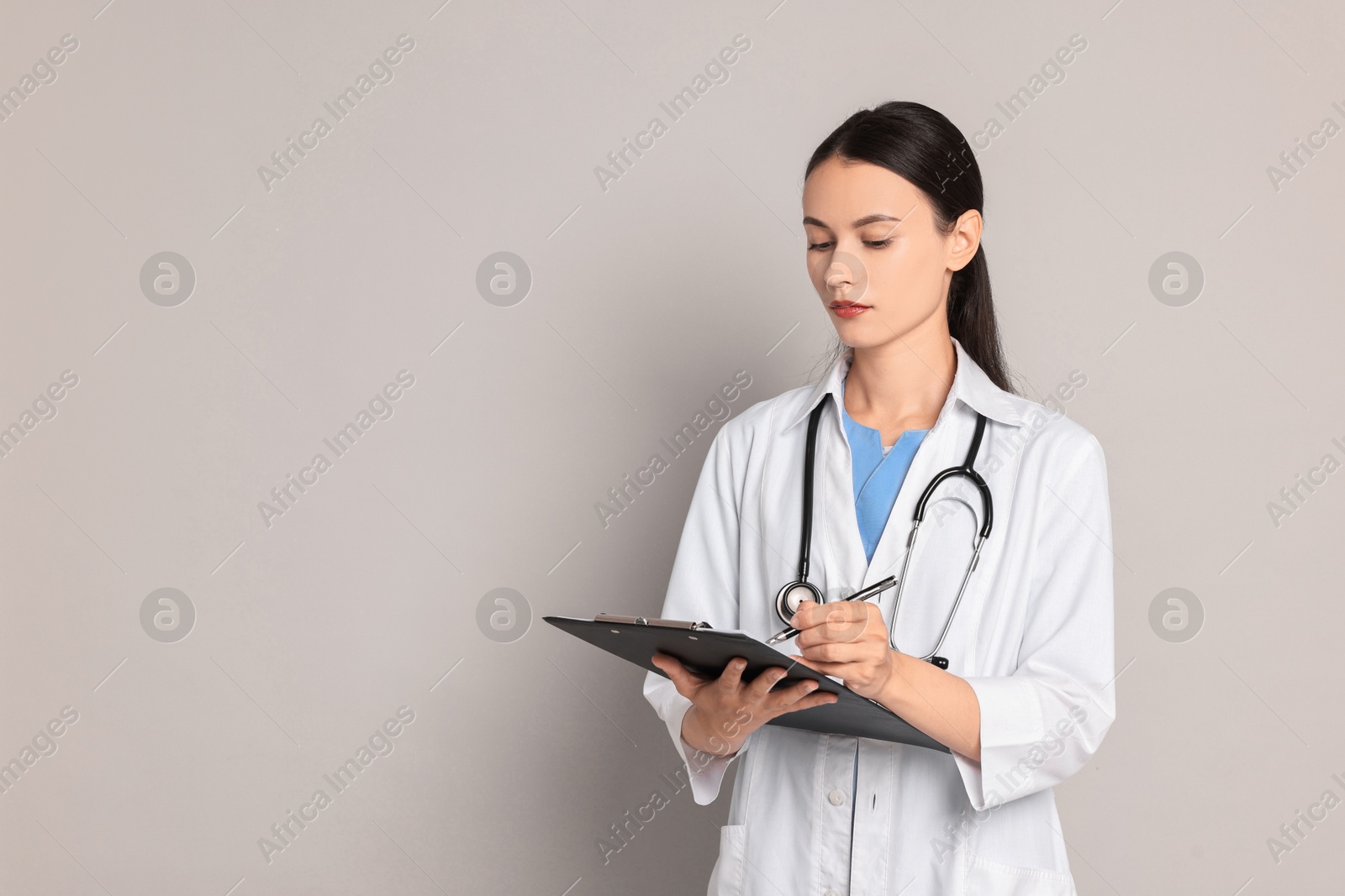 Photo of Beautiful nurse with clipboard writing notes on grey background. Space for text