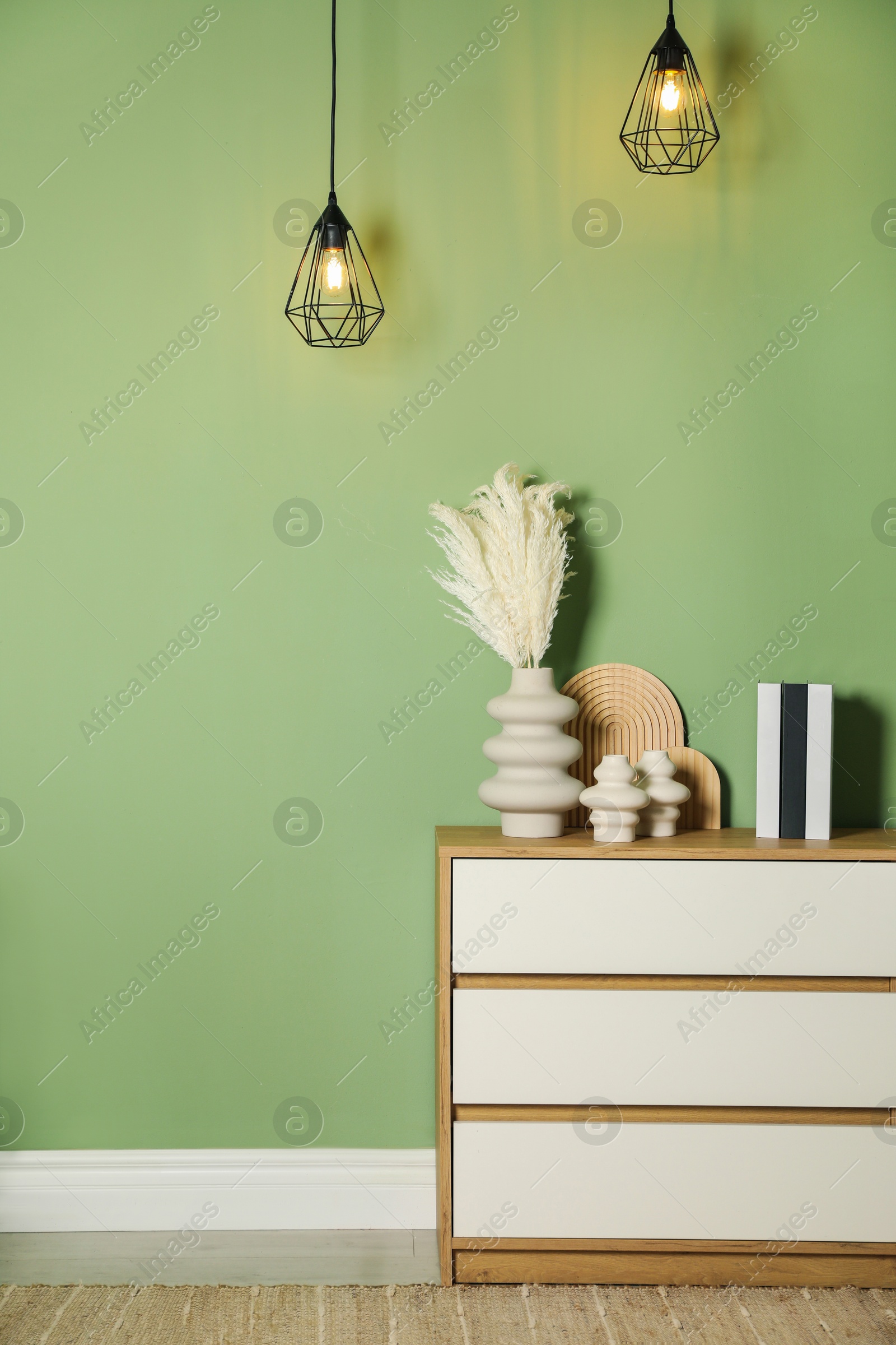 Photo of Beautiful decorative plants, vases, wooden boards and hardcover books on chest of drawers near green wall indoors, space for text