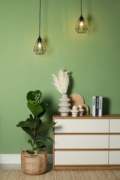 Different decorative elements on chest of drawers and houseplant near green wall indoors