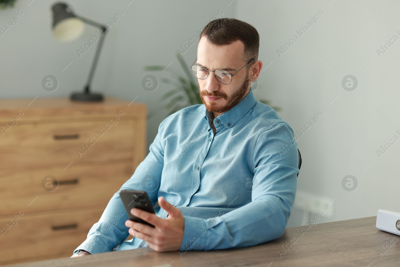 Photo of Handsome man looking at smartphone in office