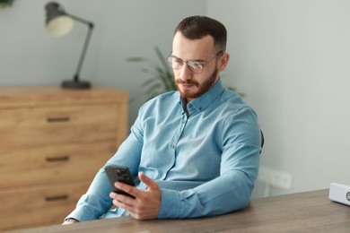 Photo of Handsome man looking at smartphone in office