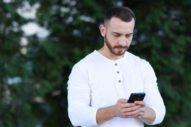 Handsome man using smartphone on blurred background. Space for text