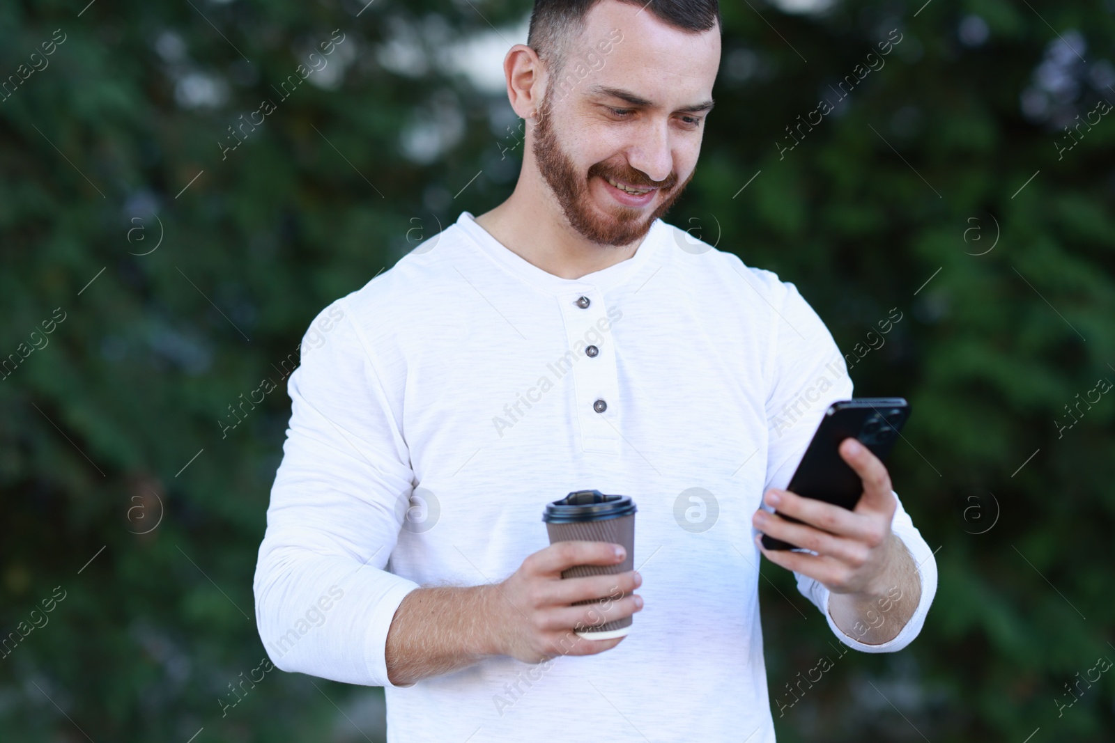 Photo of Happy man with paper cup using smartphone on blurred background