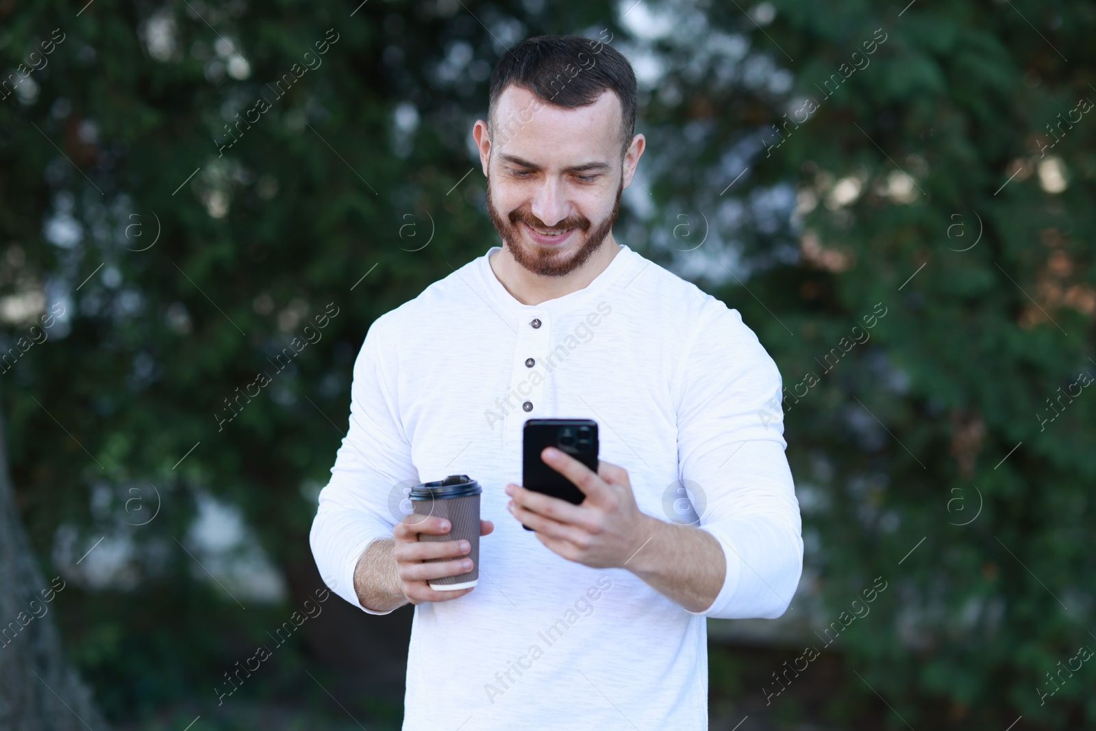 Photo of Happy man with paper cup using smartphone on blurred background