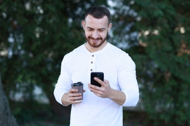 Photo of Happy man with paper cup using smartphone on blurred background