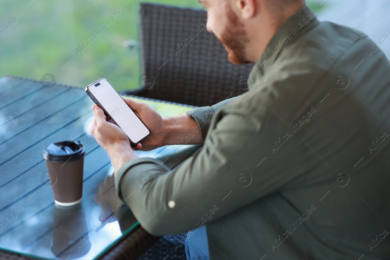 Photo of Man with paper cup using smartphone at outdoor cafe, closeup. Space for design