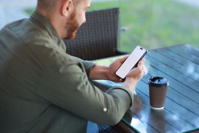 Photo of Man with paper cup using smartphone at outdoor cafe