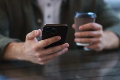 Man with paper cup using smartphone at outdoor cafe, closeup