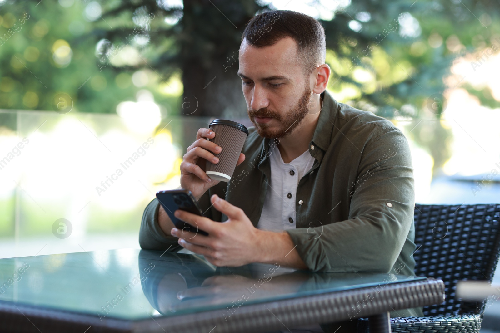 Photo of Handsome man using smartphone and drinking coffee at outdoor cafe