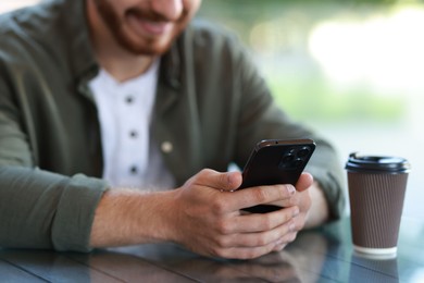 Photo of Man with paper cup using smartphone at outdoor cafe, closeup