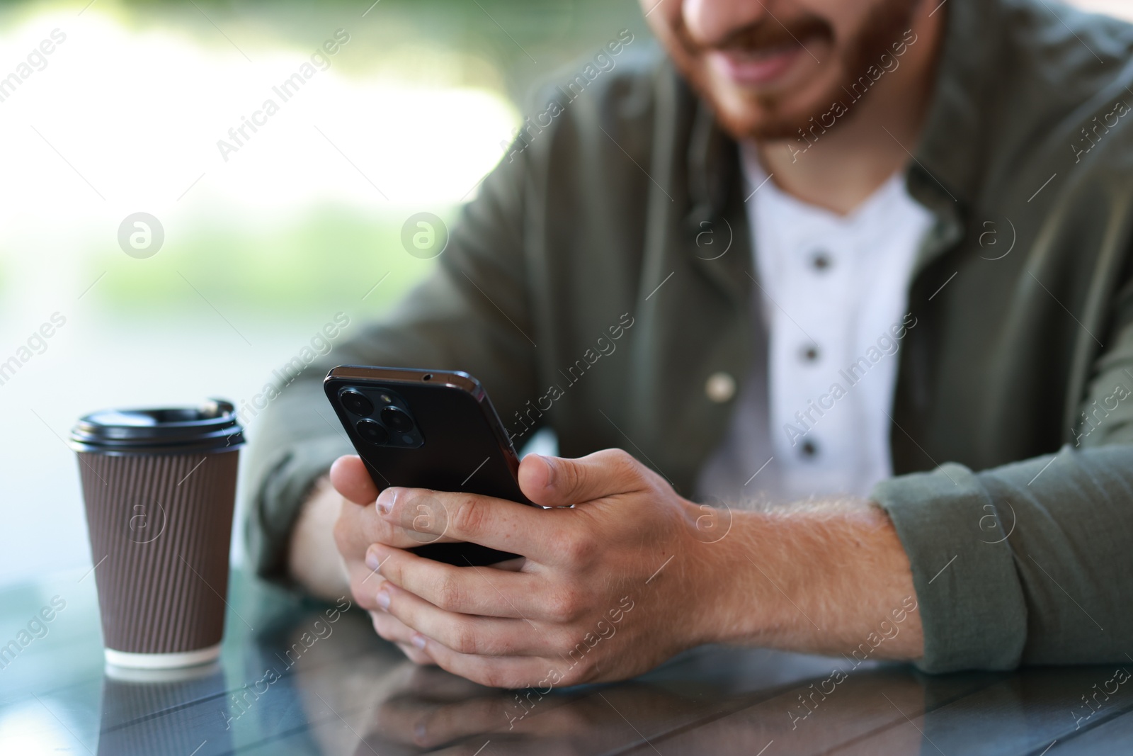 Photo of Man with paper cup using smartphone at outdoor cafe, closeup