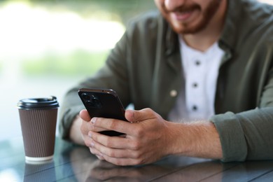 Man with paper cup using smartphone at outdoor cafe, closeup