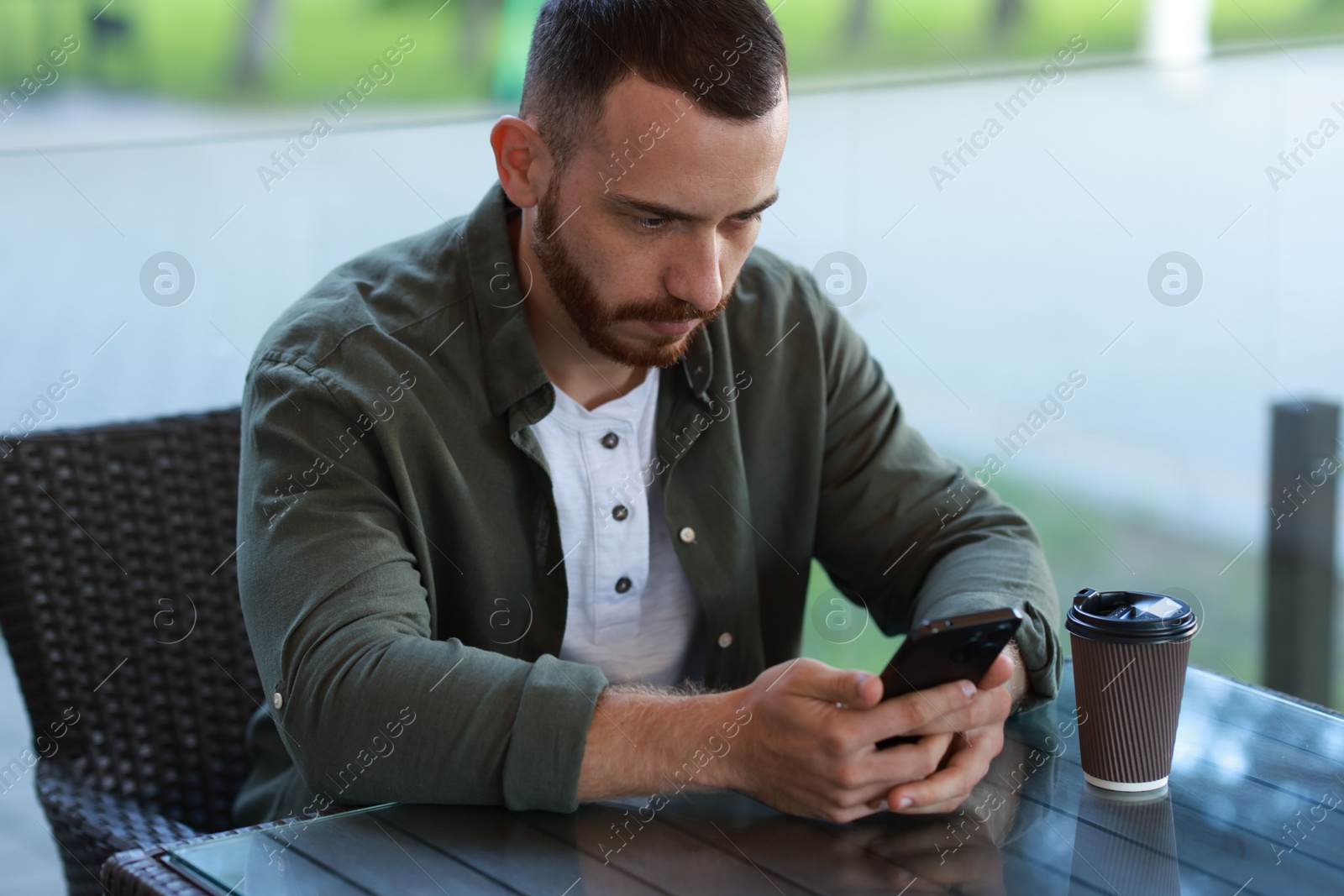 Photo of Handsome man with paper cup using smartphone at outdoor cafe