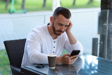 Photo of Handsome man with paper cup using smartphone at outdoor cafe