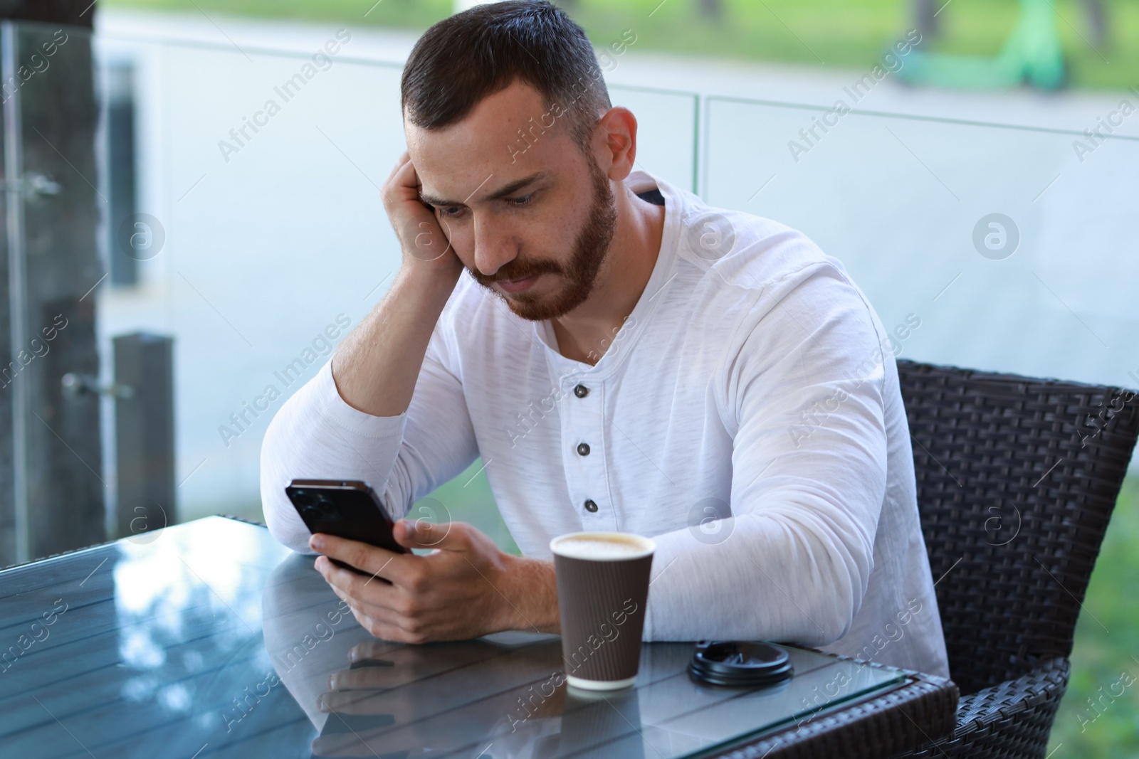 Photo of Handsome man with paper cup using smartphone at outdoor cafe