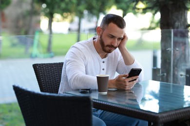 Photo of Handsome man with paper cup using smartphone at outdoor cafe