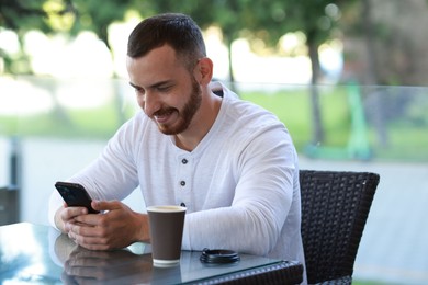 Photo of Happy man with paper cup using smartphone at outdoor cafe