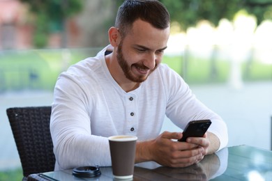 Happy man with paper cup using smartphone at outdoor cafe