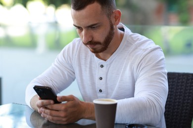 Photo of Handsome man with paper cup using smartphone at outdoor cafe