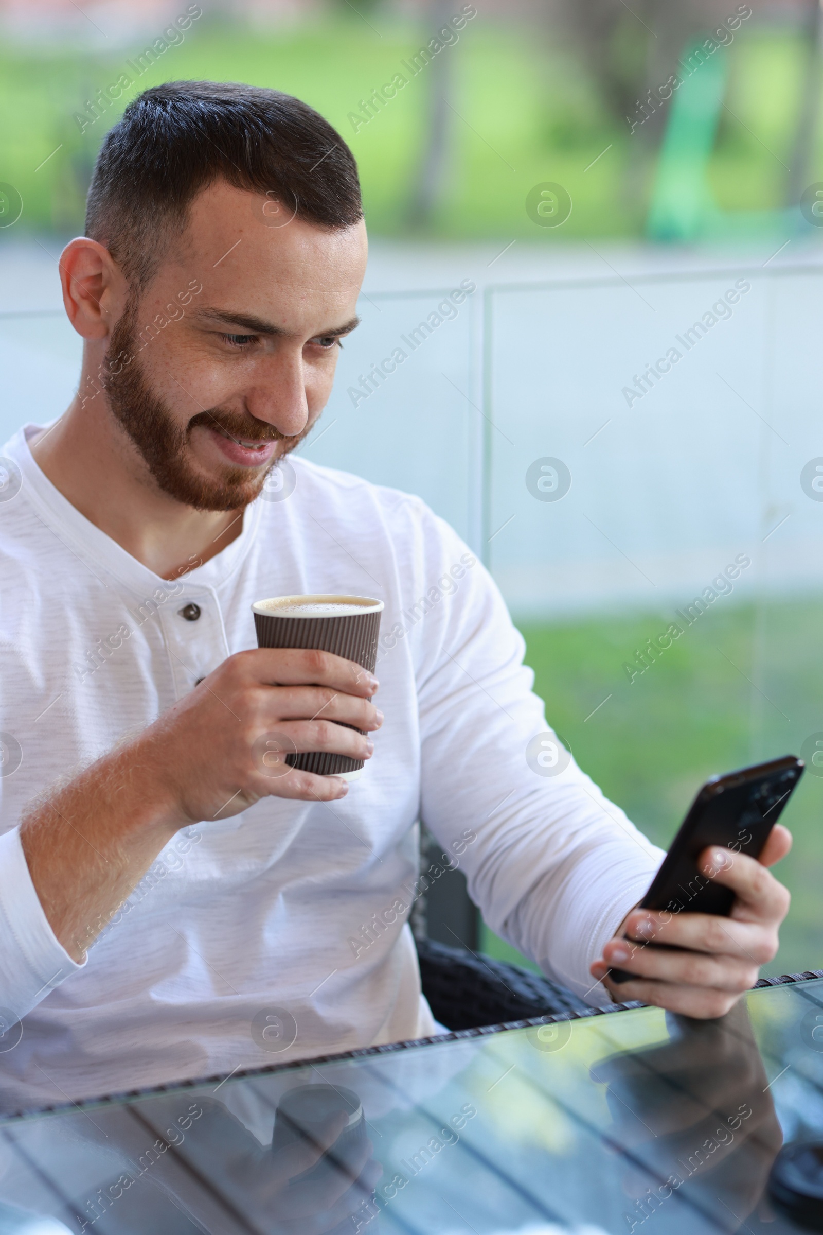 Photo of Happy man using smartphone and drinking coffee at outdoor cafe