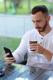 Photo of Handsome man using smartphone and drinking coffee at outdoor cafe