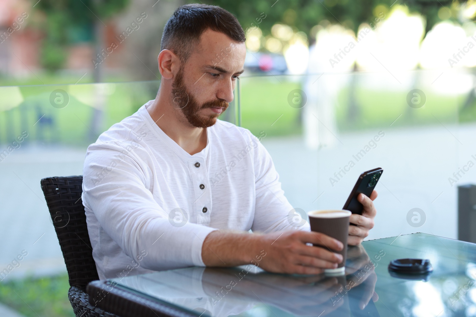 Photo of Handsome man using smartphone and drinking coffee at outdoor cafe