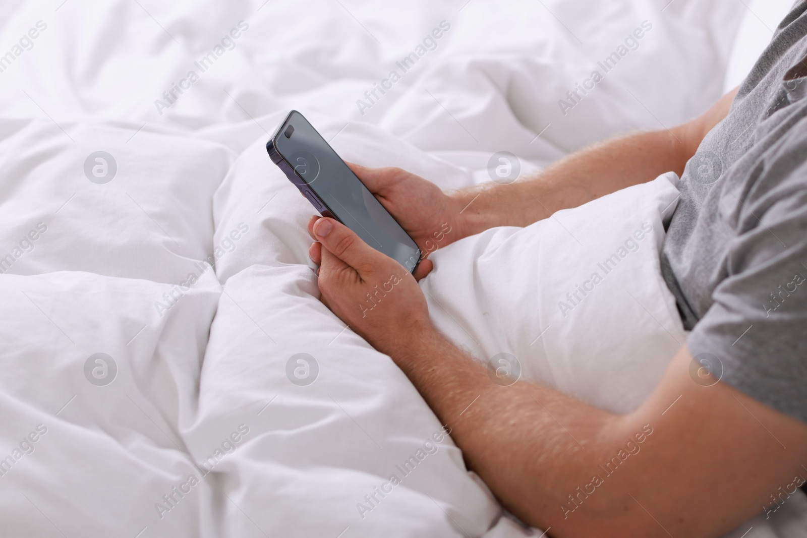 Photo of Man using smartphone in bed, closeup view