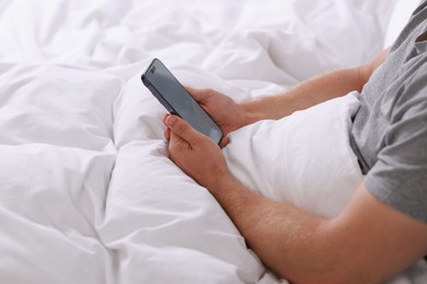 Photo of Man using smartphone in bed, closeup view