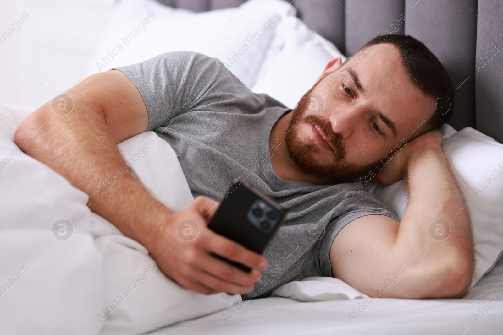 Photo of Handsome man using mobile phone in bed