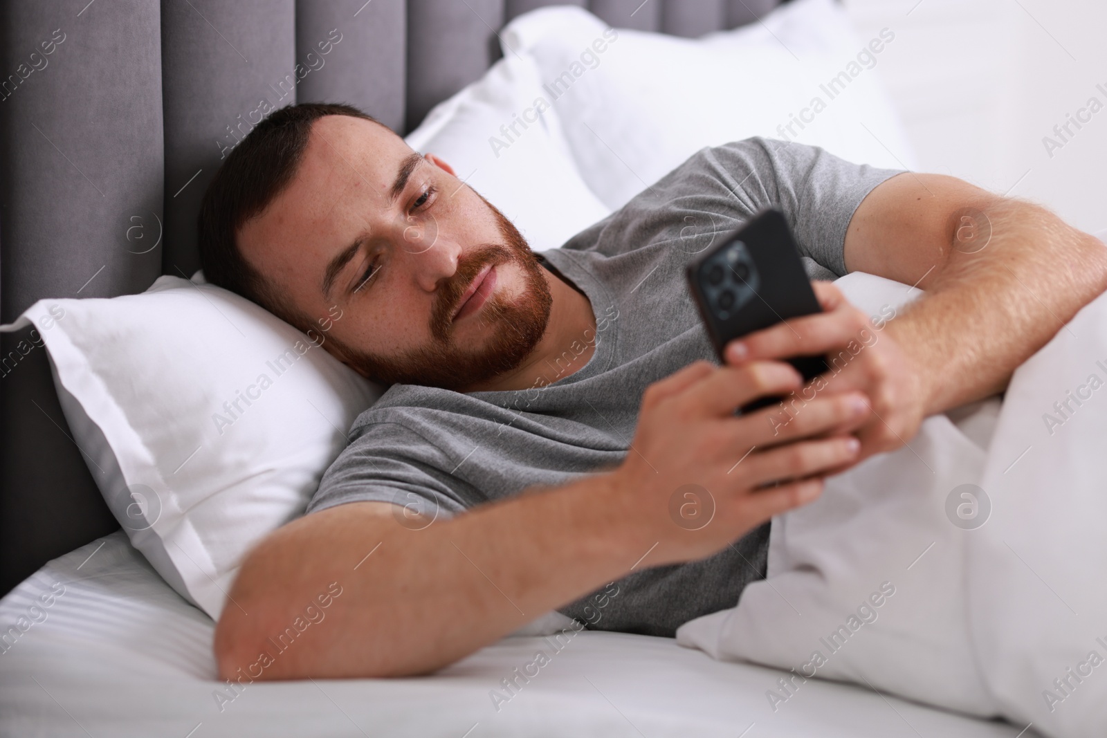 Photo of Handsome man using mobile phone in bed