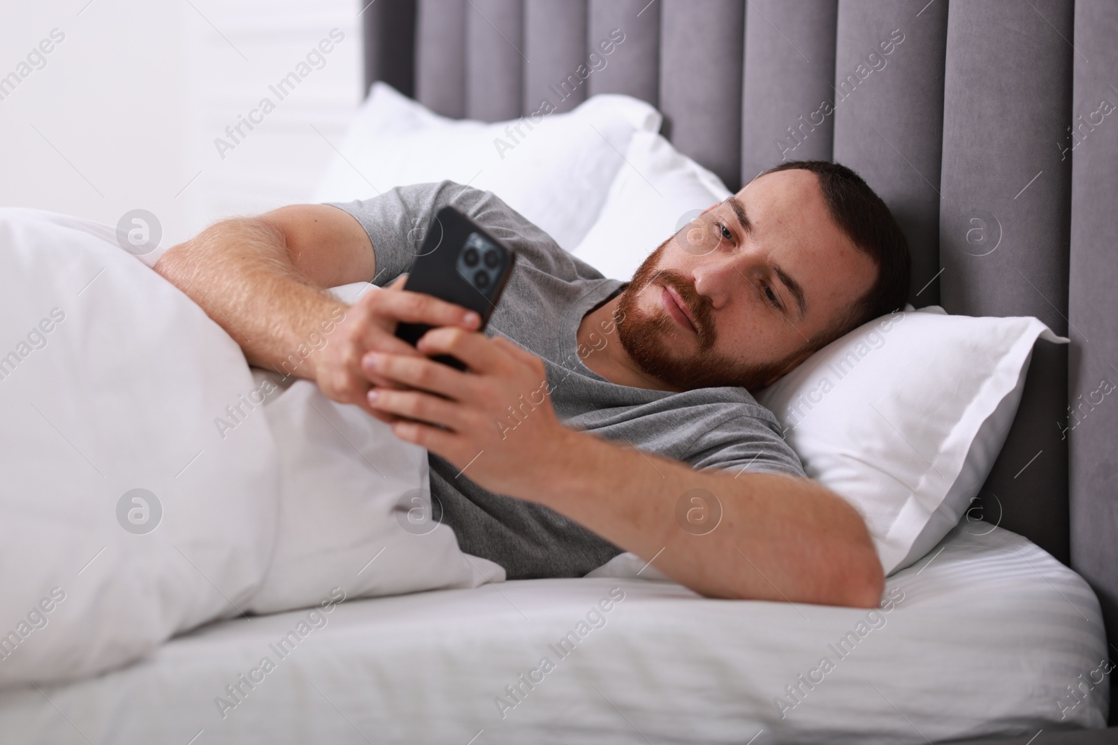 Photo of Handsome man using mobile phone in bed