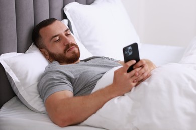 Handsome man using mobile phone in bed