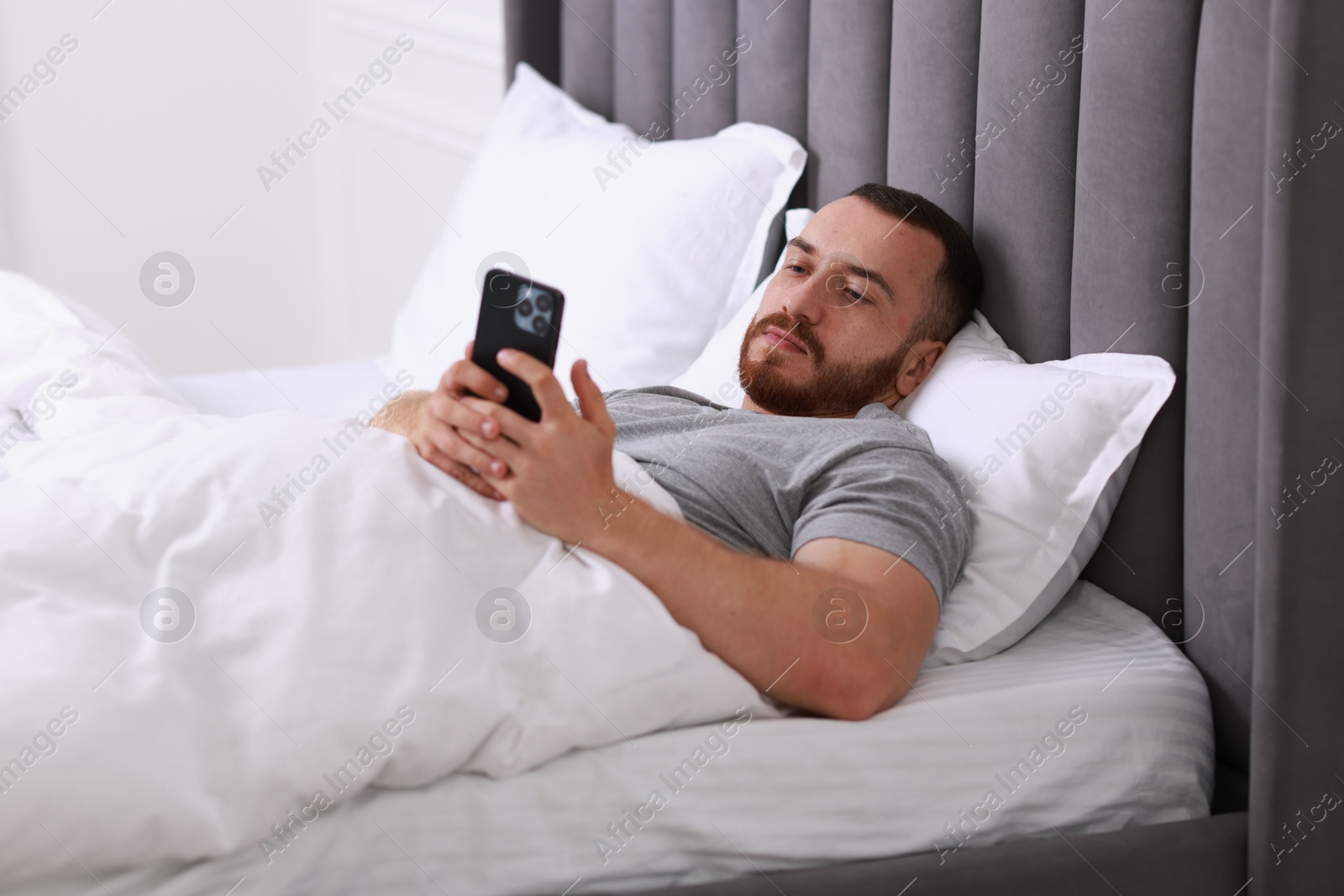 Photo of Handsome man using mobile phone in bed