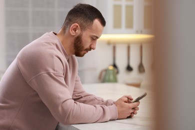 Photo of Handsome man using mobile phone in kitchen