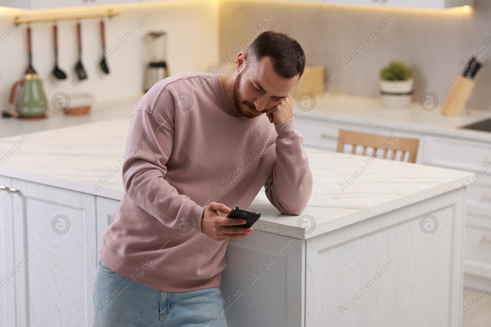 Photo of Handsome man looking at smartphone in kitchen